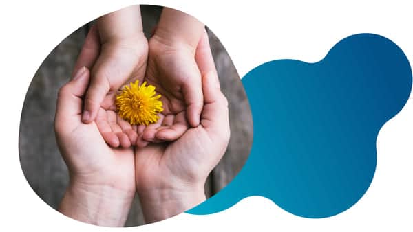 The hands of a young person holding a bright yellow flower while on top of an adult's hands