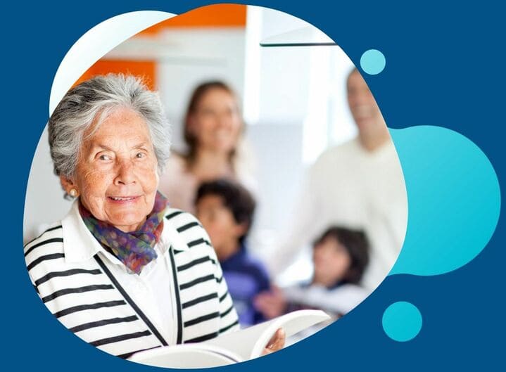 A senior citizen smiling as her family stands behind her