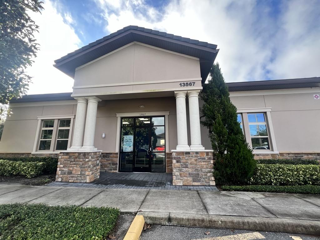 Exterior view of the Conquest Research Lake Nona building at 13567, featuring beige walls, stone accents, and white columns under a gray roof.